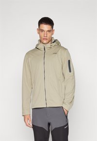 Beige jacket with hood, front zip closure, and logo detail. Features side pockets and zippered arm pocket. Worn with gray pants.