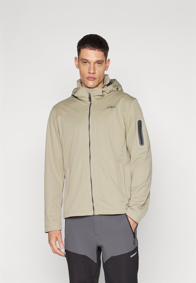 Beige jacket with hood, front zip closure, and logo detail. Features side pockets and zippered arm pocket. Worn with gray pants.