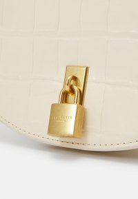 Borsa in pelle crema con motivo coccodrillo, caratterizzata da un accentuatolucchetto dorato e logo del marchio inciso. La forma è arrotondata con bordi cuciti.