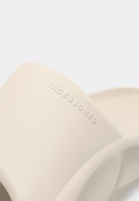 Λευκή σαγιονάρα από καουτσούκ με ανάγλυφο λογότυπο, απαλό υφή και μινιμαλιστικό σχέδιο με στρογγυλεμένες άκρες.