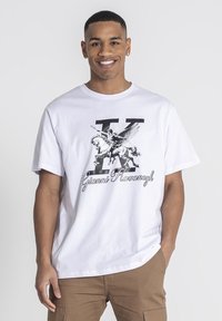 Camiseta de algodón blanca con un gráfico negro de un caballo y una figura alada, con letras en negrita "K" y "Gianni Kavanagh" impresas abajo.