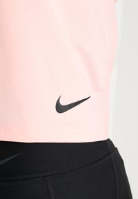 Haut de sport rose avec le logo Nike noir au-dessus de leggings noirs présentant un logo Nike assorti discret au niveau de la taille.