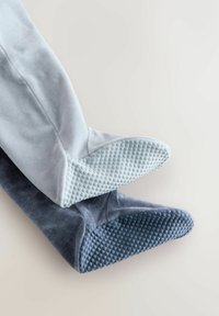 To sæt bløde, plys-sokker, ét i lyseblå med en tekstureret prikket sål, og det andet i mørkeblå med et lignende prikket sålmønster.