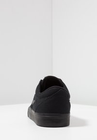 Svart canvas sneakers med låg profil, rund tå, mjuk stofft texture och svart gummisula. Har minimala sömdetaljer.