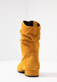 Botte en suédine jaune haute avec un design affaissé. Caractéristiques : bout rond, petit talon bloc et une languette à l'arrière pour faciliter l'enfilage.