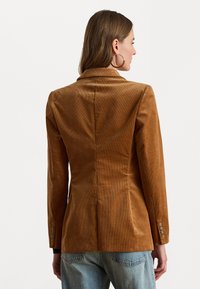 Bruine corduroy blazer met een op maat gemaakte pasvorm, notchrevers en een driedeknopdetail op de mouwen. Gladde textuur met verticale ribbels.