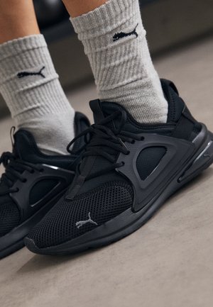 Zapatillas negras Puma con detalles de malla, usadas con calcetines Puma gris claro, pies colocados sobre una superficie de suelo lisa.
