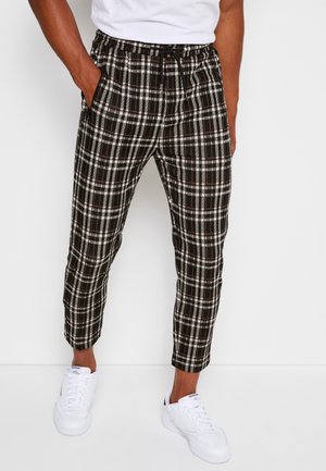 Pantalons à carreaux noir et blanc avec une taille élastique et des poches latérales, présentant un design de jambe fuselée, associés à des baskets blanches.