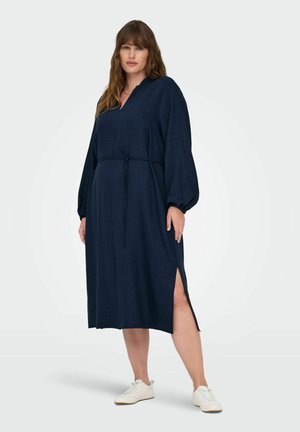 Marinblå midi-klänning med långa ballongärmar, knytmidja och sidoklipp. Tillverkad av textil med struktur. I kombination med vita sneakers.