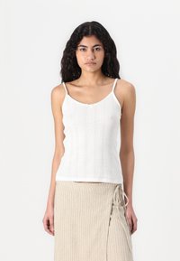 Weißes, geripptes Trägershirt mit dünnen Schulterträgern und einem kleinen Schleifendetail in der Mitte. Es hat ein strukturiertes Muster entlang des Körpers.
