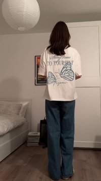 Tricou alb supradimensionat, cu ilustrații de fluturi albaștri și text pe spate. Asortat cu blugi albaștri cu picioare largi.