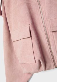 Mäkká ružová bunda na zapínanie na zips s veľkými klopovými vreckami na prednej strane a viditeľným strieborným zipsom na svetlom pozadí.