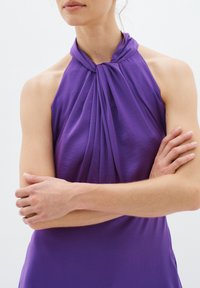 Rochie lilac cu guler tip halter, având un front drapat și o textură netedă. Designul fără mânecă evidențiază umerii și brațele, având un detaliu legat la gât.