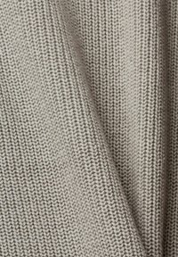 Tessuto a maglia testurizzato di colore grigio chiaro, con cuciture evidenti e un motivo morbido e uniforme. Il materiale appare spesso e accogliente.