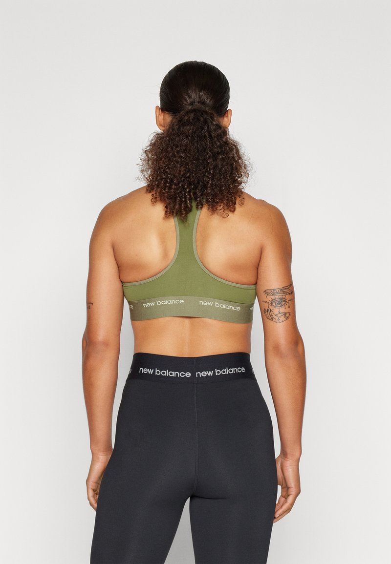 Olivgrüner Sport-BH mit Racerback-Design, ausgestattet mit einem Markenband. Kombiniert mit hochgeschnittenen schwarzen Leggings, glatte Textur.