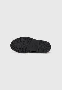 Black rubber boot sole featuring a rugged tread pattern with circular and rectangular grips for enhanced traction and durability.