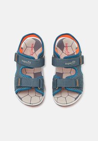 Blå og grå åpne sandaler med justerbare stropper, teksturerte såler med geometrisk mønster, og kontrasterende oransje aksenter.