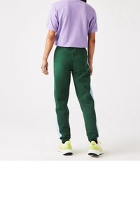 Gröna joggers med ljusblå sidopaneler, parat med en lila t-shirt med kort ärm. Sneakers är gula med mörka sulor och detaljer.