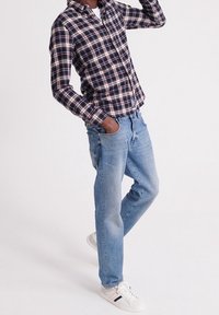 Camicia a quadri con bottoni in blu navy, rosso e crema; jeans di denim azzurro chiaro; sneakers bianche con dettagli neri e rossi. Outfit casual mostrato.