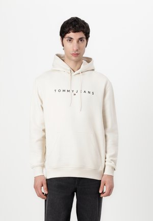 Crèmekleurige hoodie met een voorzak, capuchon met trekkoord en het "TOMMY JEANS" logo in het zwart over de borst. Zachte stof, relaxed fit.