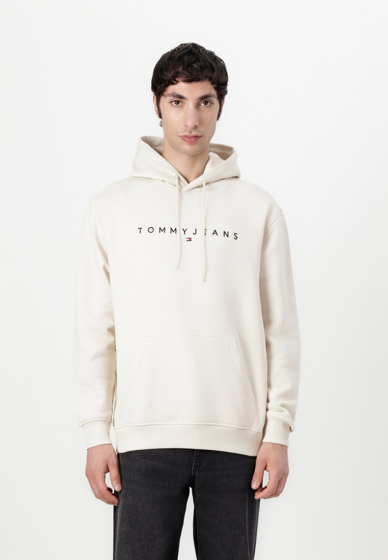 Crèmekleurige hoodie met een voorzak, capuchon met trekkoord en het "TOMMY JEANS" logo in het zwart over de borst. Zachte stof, relaxed fit.