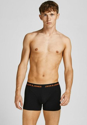 Shirtless man wearing black boxer briefs with "JACK & JONES" orange logo waistband, standing against a plain light gray background.