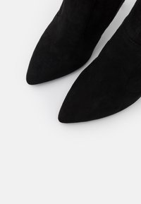 Svarta mockaankleboots med en spetsig tådesign. Texturen är mjuk och har en slank silhuett samt en enkel, minimalistisk estetik.