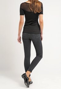 Černý přiléhavý top s krátkými rukávy a průhledným zadním dílem, kombinovaný s černými skinny džínami a černými botami. Jednoduchý a elegantní design.