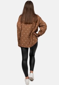 Brown, oversized shirt with white heart patterns, textured fabric, and long sleeves, paired with black, shiny leggings and white sneakers.