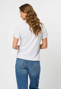 Hvit ribbet kortermet polo skjorte med en tettsittende design, kombinert med medium-vaskede blå jeans. Subtil logo detalj på ermene.
