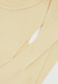 Tessuto a maglia a coste beige con dettaglio a taglio, caratterizzato da una superficie texturizzata e bordi leggermente sfilacciati. Il design comprende sezioni sovrapposte.