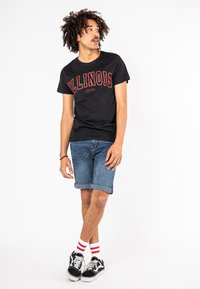 Zwart T-shirt met korte mouwen met rode tekst "ILLINOIS", gecombineerd met opgerolde denim shorts en zwarte sneakers met witte en rode gestreepte sokken.