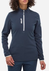 Dunkelblauer Pullover mit einem Viertelreißverschluss, ausgestattet mit strukturiertem Stoff und weißem Logo. Lange Ärmel mit kontrastierenden weißen Bündchen.