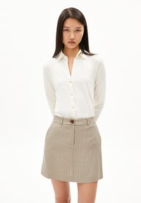 Witte button-up blouse met lange mouwen, gecombineerd met een beige geruite rok met een knoop aan de voorkant en riemlussen. Schoon ontwerp, lichtgewicht stof.