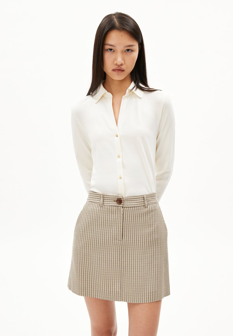 Witte button-up blouse met lange mouwen, gecombineerd met een beige geruite rok met een knoop aan de voorkant en riemlussen. Schoon ontwerp, lichtgewicht stof.