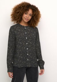 Blouse à boutons florale avec un fond bleu foncé et des motifs floraux verts et blancs. Manches longues et col rond.