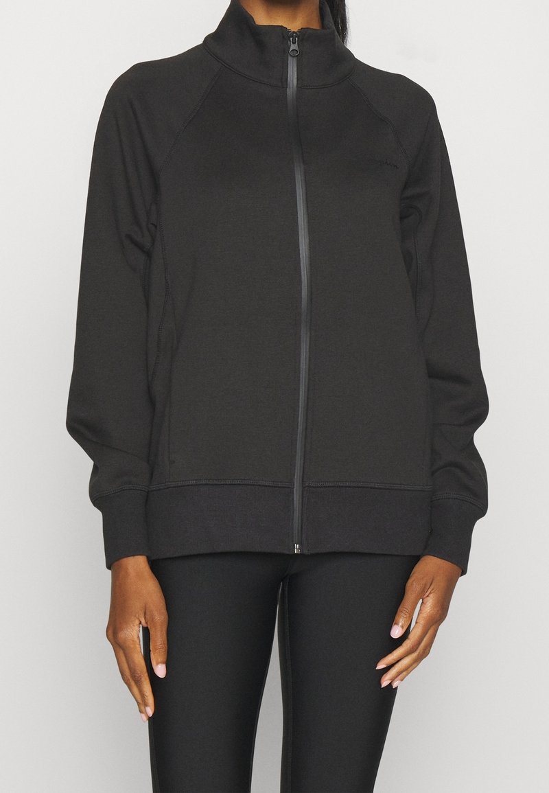 Svart zip-up jacka i mjukt, texturerat tyg med hög krage, raglanärmar och ribbade muddar. Stylar med slim fit svarta byxor.