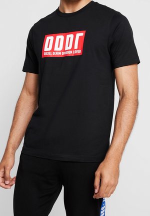 Mężczyzna ubrany w czarną koszulkę z krótkim rękawem z czerwono-białym logo „DDDL Diesel Denim Division Lover” na piersi na jednolitym tle.
