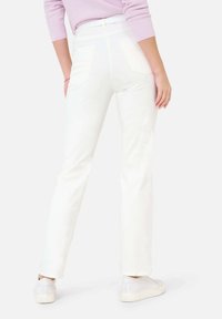 Pantalons droits blancs avec poches, présentant une texture lisse et une taille haute. Associés à des baskets blanches et un haut violet clair.