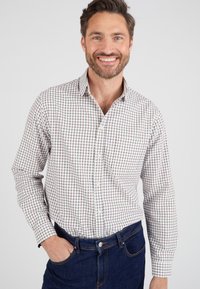 Camicia bianca a scacchi con motivo a griglia blu e rossa, colletto button-down, maniche lunghe e taschino; abbinata a jeans in denim scuro.