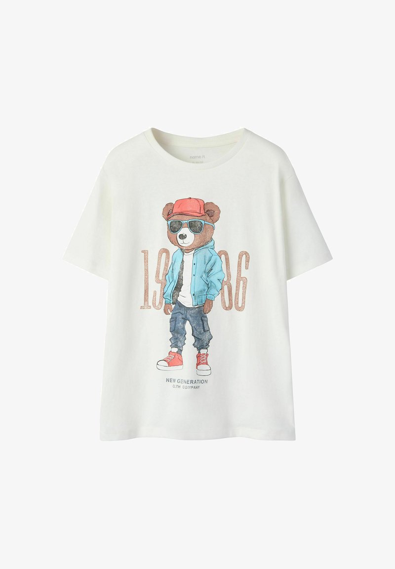 T-shirt blanc avec un graphisme d'un ours portant une casquette rouge, une veste bleu, des lunettes de soleil, un jean et des baskets rouges avec les textes "1986" et "Nouvelle Génération".