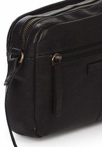 Bolso de hombro negro de cuero con cremallera en la parte superior, bolsillo frontal y correa desmontable. Presenta costuras sutiles y herrajes en tono dorado.