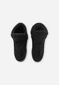 Zapatillas negras de material suave con superficie texturizada, acentuadas con pequeñas tachuelas. Presentan una puntera redonda y un forro acolchado. Diseño casual.