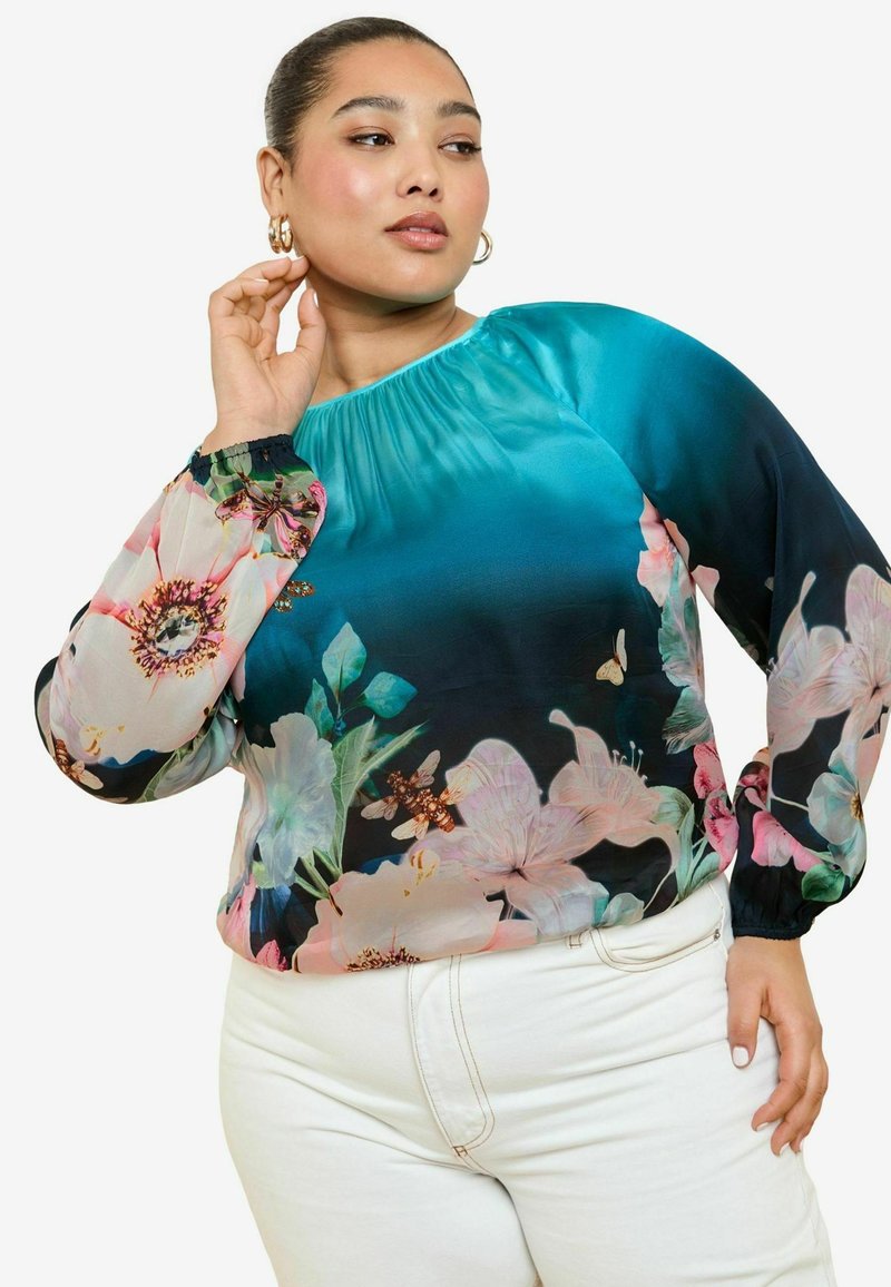 Blusa floreale in gradiente blu e nero con maniche lunghe e trasparenti, decorate con fiori rosa e farfalle. Scollatura arricciata e polsini elasticizzati.