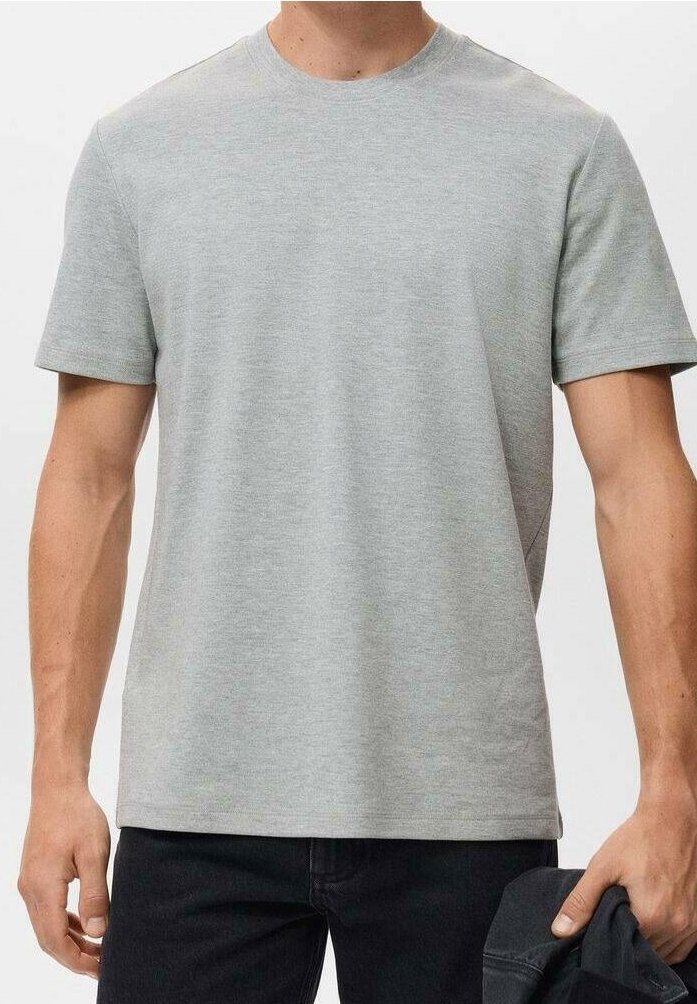 Homme portant un t-shirt uni gris clair à manches courtes et un pantalon foncé, tenant une veste sombre dans sa main droite.