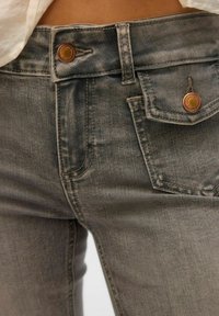 Grå denimbukser med kobberdetaljer, en knaplukning og for- lommer. Stoffet viser let udtoning og en glat tekstur.