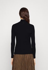 Zwarte geribbelde lange mouwen top met een opstaande kraag, aansluitend ontwerp en subtiele logo-detail nabij de halslijn, gecombineerd met een patroonrok.