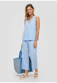 Top senza maniche blu chiaro con dettaglio a fiocco; abbinato a pantaloni larghi blu chiaro. Accentuato da una borsa a tracolla a righe blu e sandali beige.