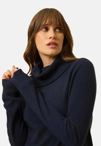 Marineblaues Rollkragensweatshirt mit einer weichen Textur, das einen lockeren Schnitt und lange Ärmel aufweist, akzentuiert durch ein breites Kragen-Detail.