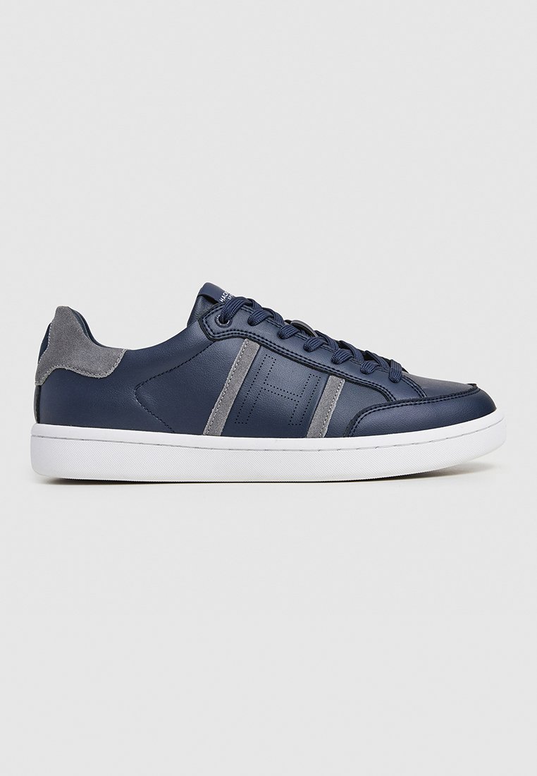 Baskets en cuir bleu marine avec des accents en daim gris, design à lacets, semelle en caoutchouc blanche, et rayures horizontales empilées sur les côtés.